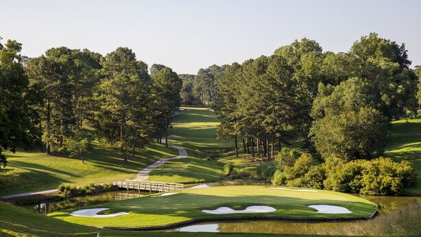 Un campo de golf con un obstáculo acuático, búnkeres de arena y un puente.