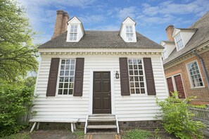 Un bâtiment blanc avec une porte et des volets marron foncé, un petit porche à l’avant et une cheminée.