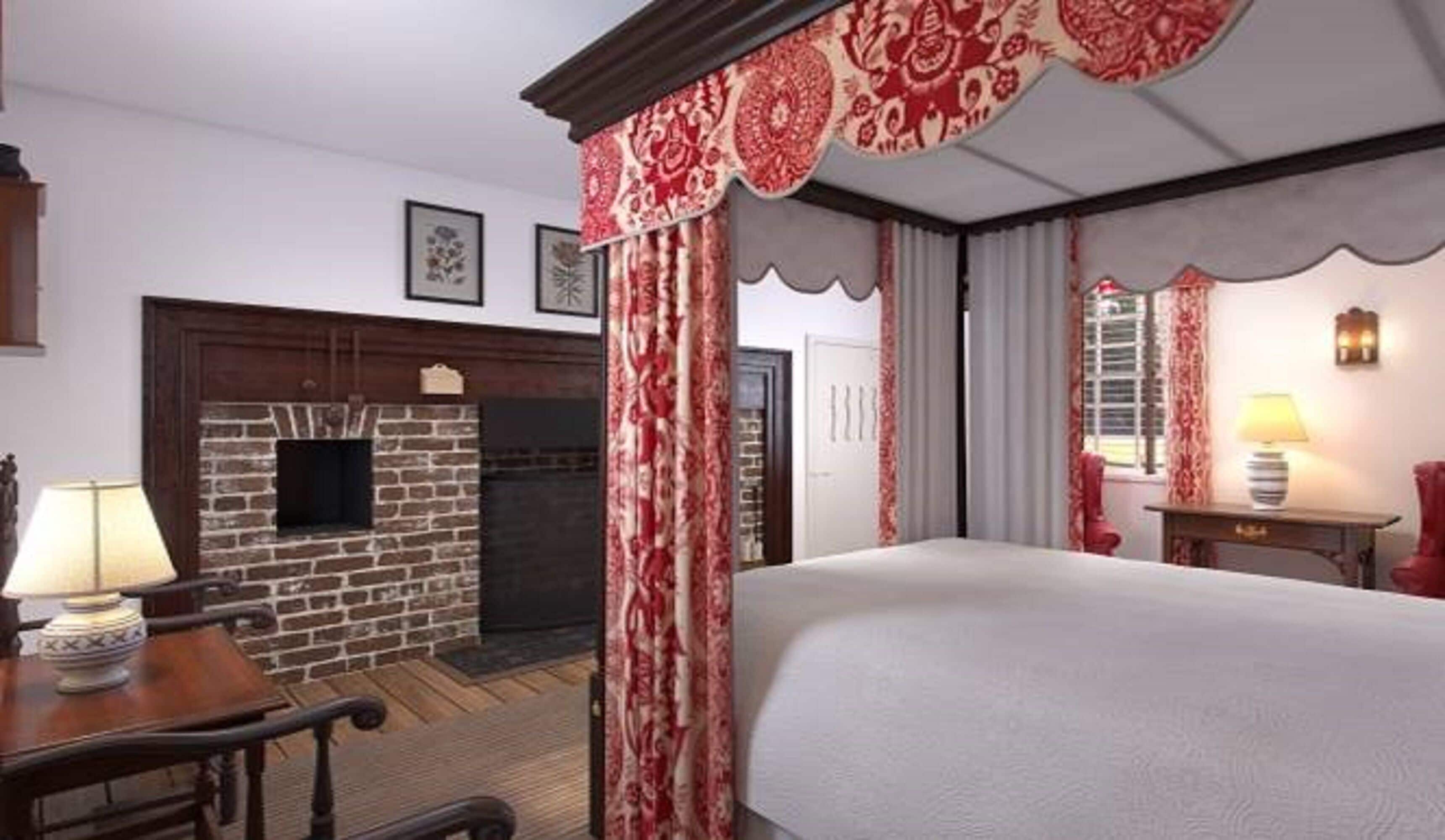 A hotel room with a fireplace, a bed, a desk with a lamp, and a window with curtains.
