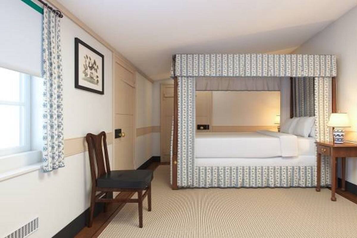 A hotel room with a bed, a chair, a bedside table with a lamp, and a window with curtains.