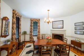Une salle à manger avec une table en bois, des chaises, un lustre, une cheminée et des tableaux encadrés accrochés au mur.