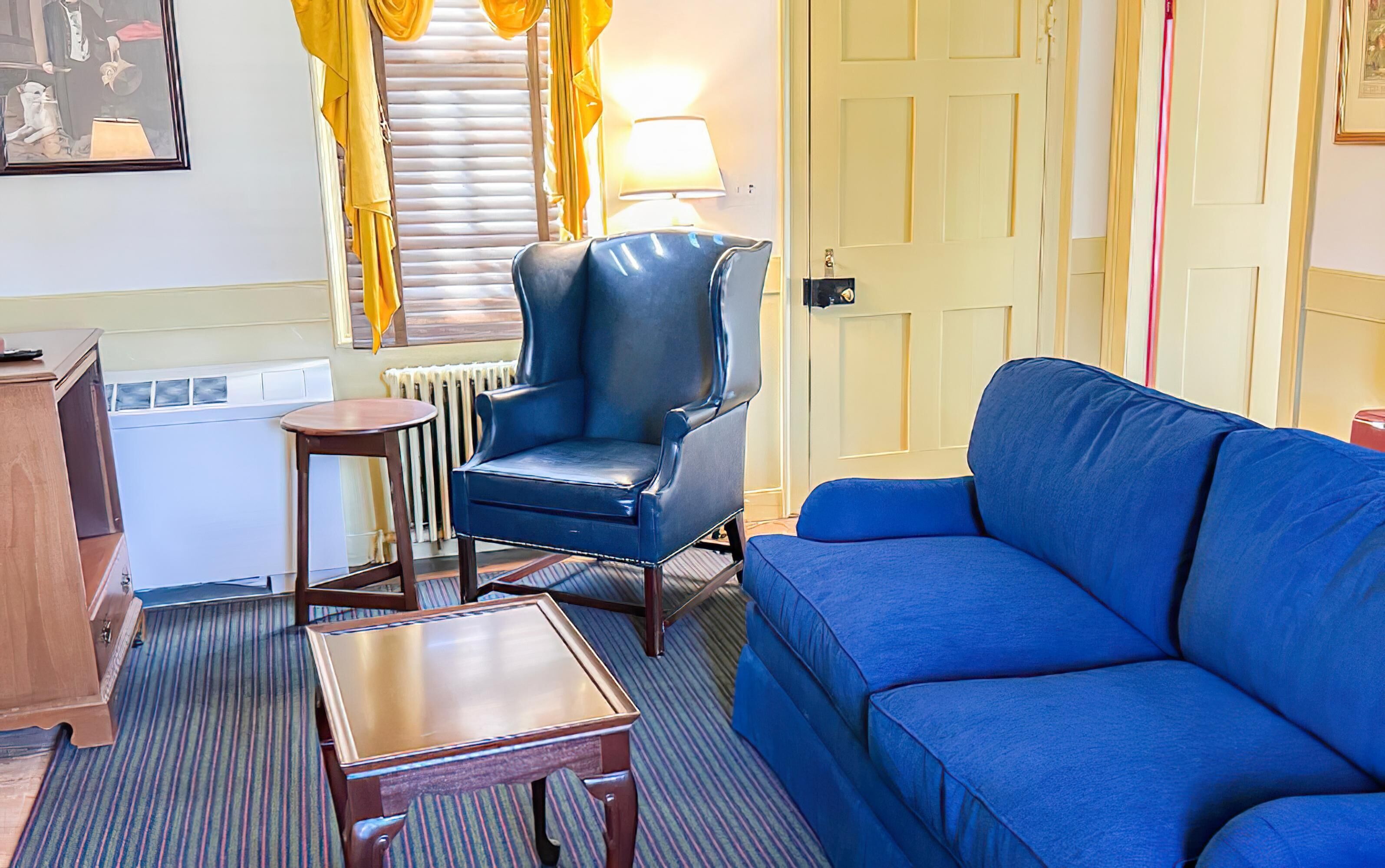 A room with a blue sofa, a leather armchair, a small wooden table, and a radiator.