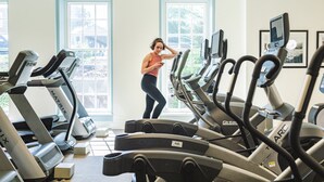 Un gimnasio con varias cintas de correr, una persona usando una cinta y amplias ventanas con vistas a zonas verdes.