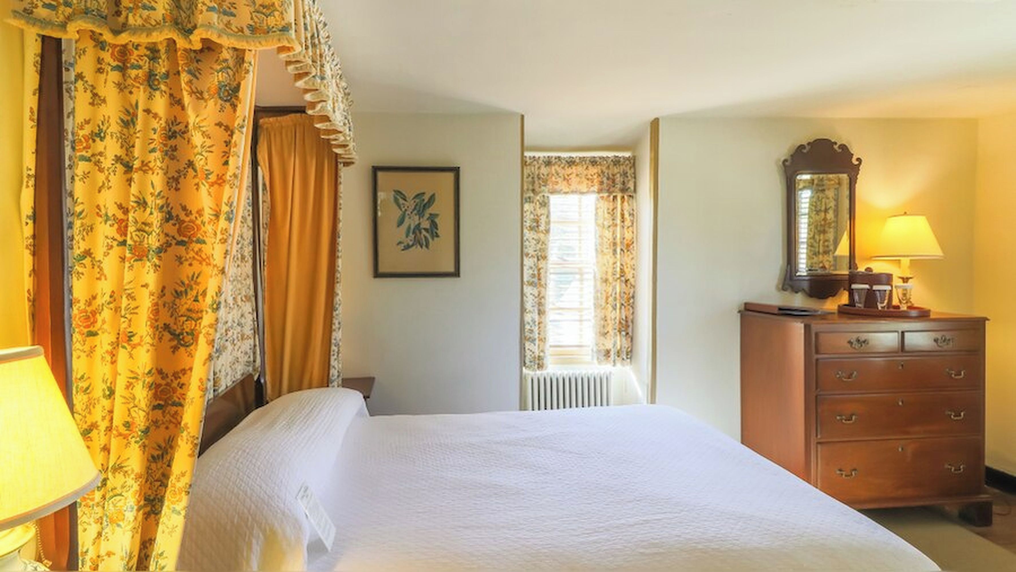 Una habitación de hotel con una cama, un tocador, un espejo y una ventana con cortinas.