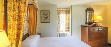 Una habitación de hotel con una cama, un tocador, un espejo y una ventana con cortinas.