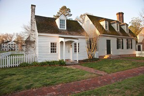 Une maison blanche de style colonial, avec un chemin en briques et une clôture en bois peinte en blanc.