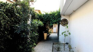 A narrow alleyway with dense foliage on one side and a building entrance on the other. - Villa Tata Suites (Curitiba)
