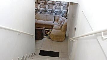 Una escalera conduce a una sala de estar con un papel tapiz estampado y un sofá color beige.