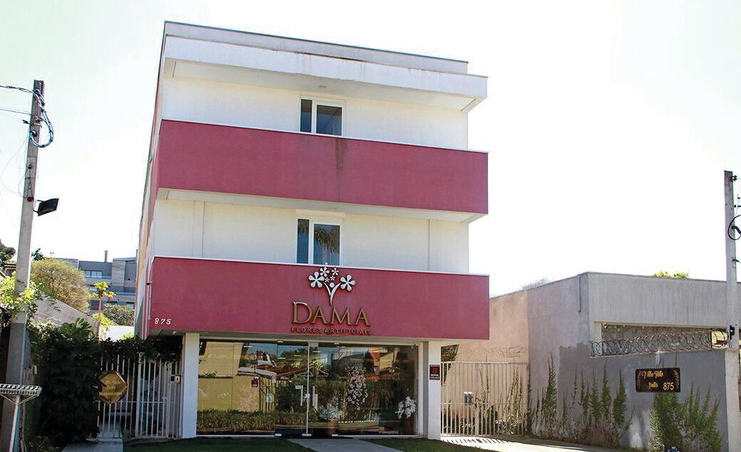 A two-story building with a red and white facade, featuring a storefront with the name "DAMA" and the text "Florecs Artificiels".