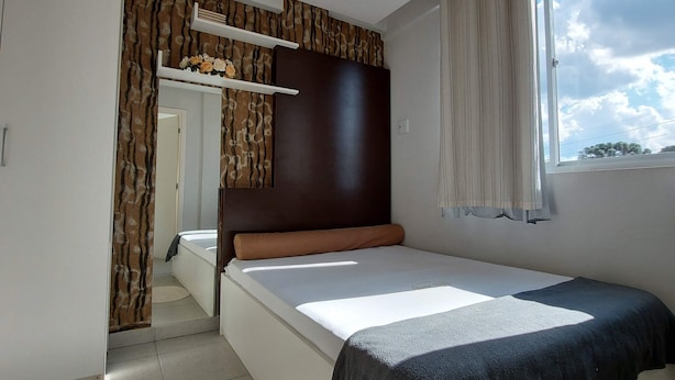 A bedroom with a bed, a window, a mirror, and a wardrobe. - Villa Tata Suites (Curitiba)
