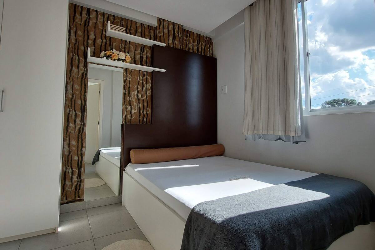 A bedroom with a bed, a window, a mirror, and a wardrobe.