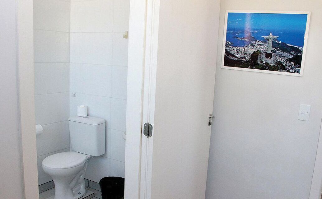 A bathroom with a toilet, a white door, and a picture of Christ the Redeemer on the wall.