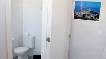 A bathroom with a toilet, a white door, and a picture of Christ the Redeemer on the wall.