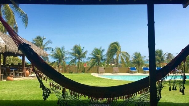 A hammock under a thatched roof, a pool, palm trees, and lounge chairs. - Pousada Point Break (Caucaia)