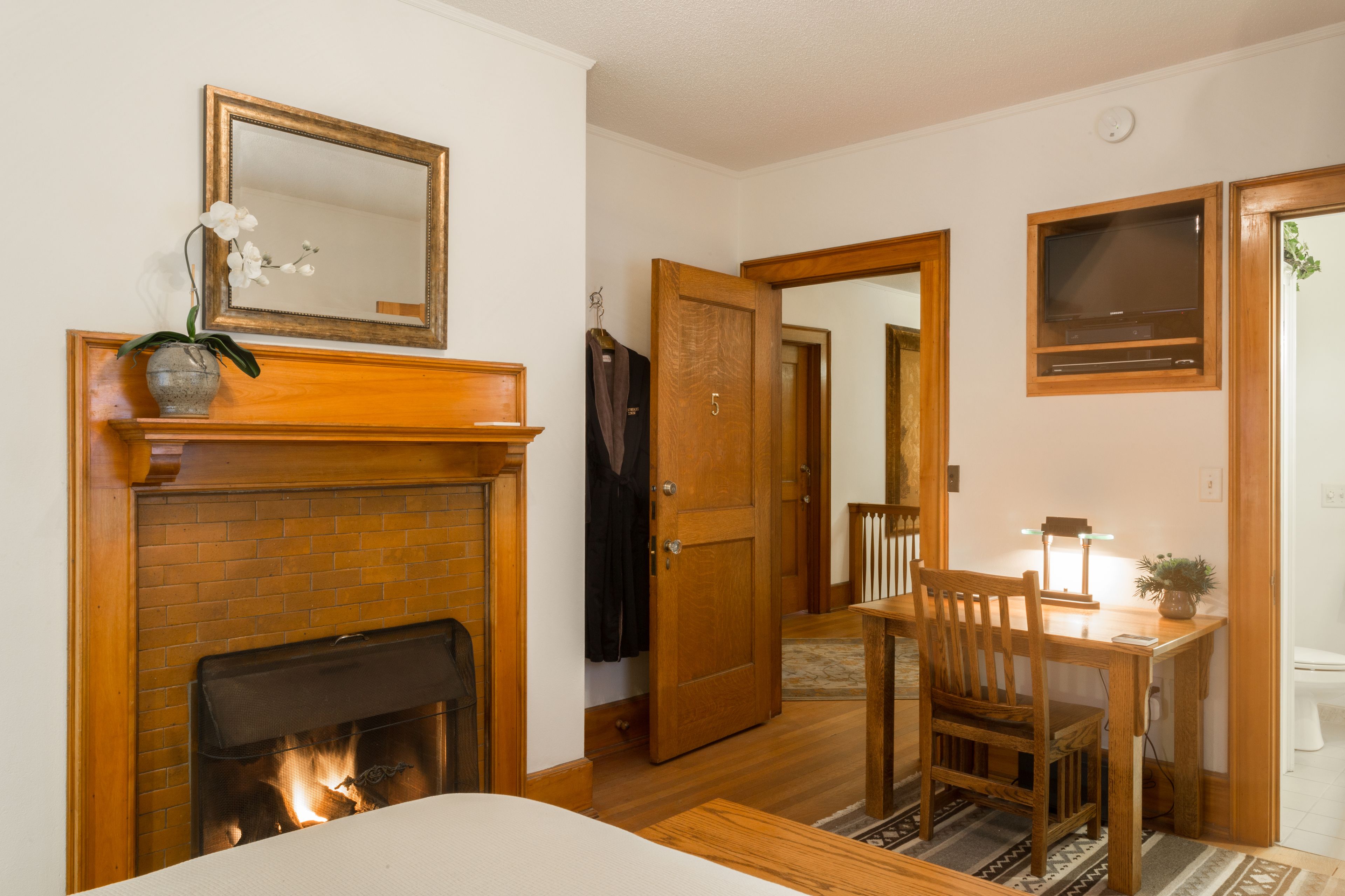 Une pièce avec une cheminée, une table en bois avec une chaise, un miroir et une porte donnant sur une autre pièce.