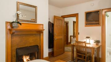 Une pièce avec une cheminée, une table en bois avec une chaise, un miroir et une porte donnant sur une autre pièce.