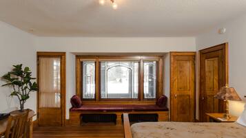 A bedroom with a wooden bench by the window, a bed with a floral bedspread, and a lamp on a bedside table.