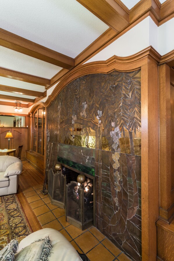 A cozy living room with a fireplace, wooden beams, and a patterned wall.