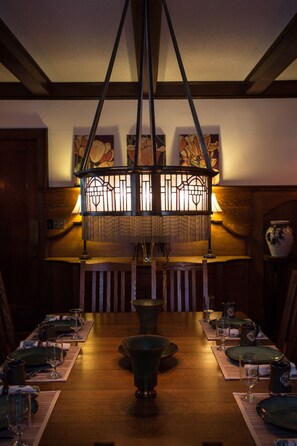 A dining area with a wooden table set for a meal, a hanging light fixture, and artwork on the walls.