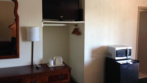 Quarto de hotel com cômoda de madeira, televisão de tela plana na parede, micro-ondas em um armário e cabideiro.