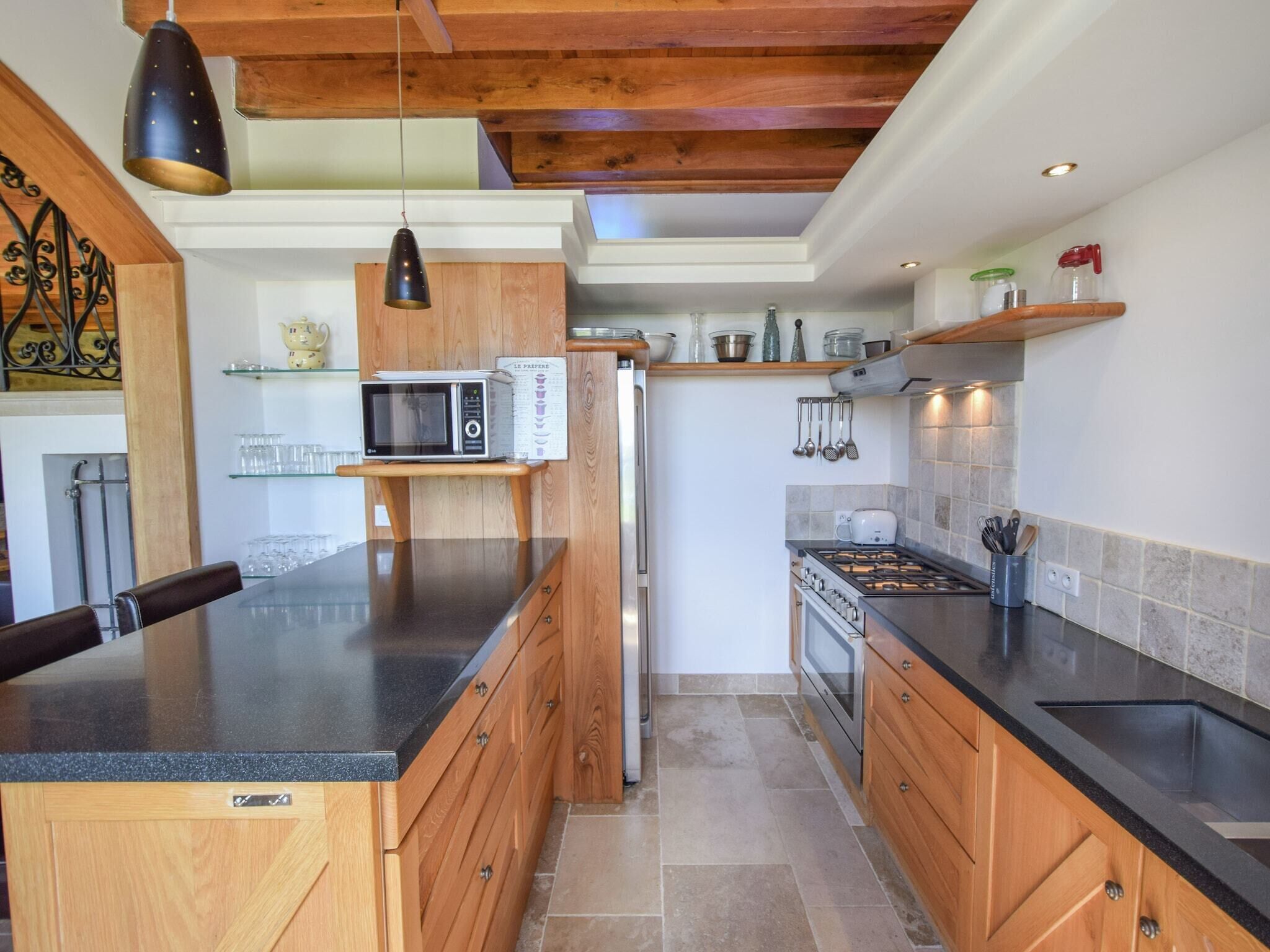 Une cuisine moderne avec des meubles en bois, un plan de travail noir, un four à micro-ondes, un réfrigérateur, une cuisinière et un porte-casseroles suspendu.