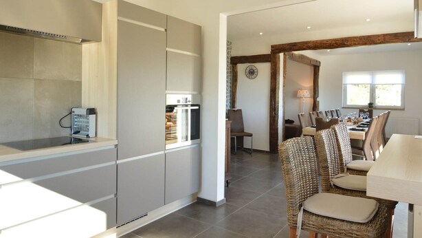 A modern kitchen with built-in appliances, a dining area with wicker chairs, and a rustic wooden beam ceiling. - Villa with Spa-Francorchamps F1 Circuit (Francorchamps (Stavelot))