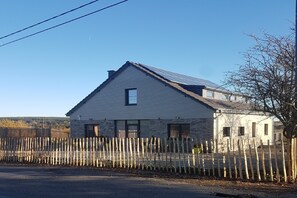 Une maison à deux étages, avec un toit en pente, une petite fenêtre et une clôture en bois à l’avant.