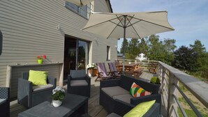 An outdoor patio with wicker furniture, a large umbrella, and a view of a house in the background. - Villa with Spa-Francorchamps F1 Circuit (Francorchamps (Stavelot))
