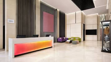 A modern hotel reception area with a reception desk, seating area, and a large screen.