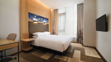 Una habitación de hotel con una cama, un escritorio, una silla, un televisor de pantalla plana y una obra de arte con vista a la ciudad.