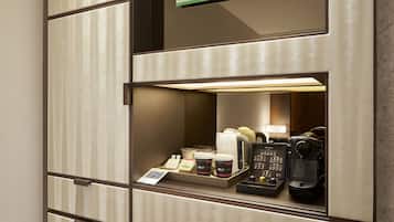 Habitación de hotel con minibar que contiene cafetera, tazas y una bandeja con artículos de desayuno.