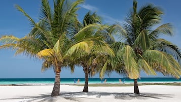 Na praia, areia branca, espreguiçadeiras, toalhas de praia 