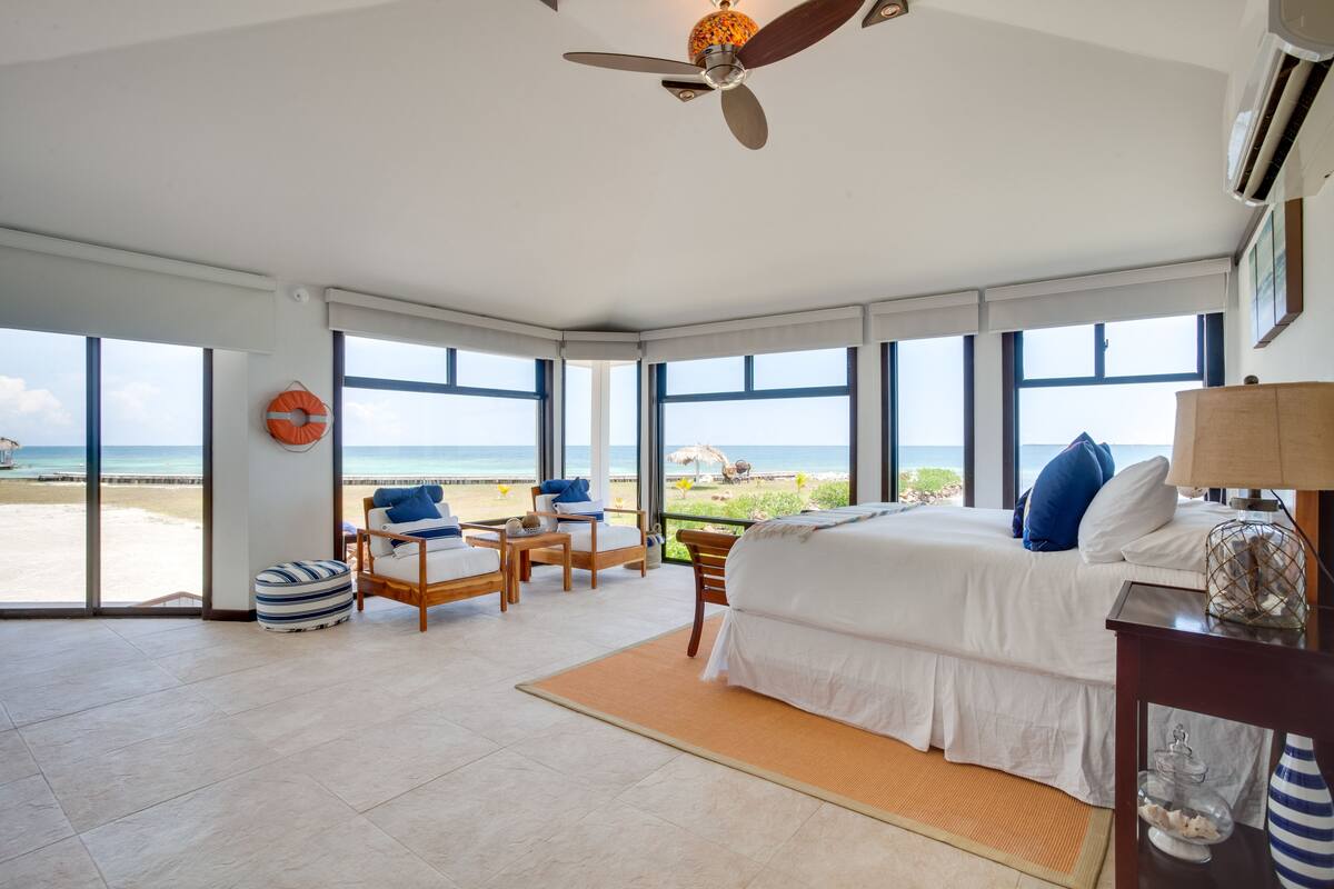 A spacious bedroom with a large bed, a ceiling fan, and a view of the beach.