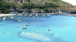 A coastal area with boats on clear blue water, a hillside, and a building with a white facade. - Romantic Escape w/ Terrace (Palinuro)