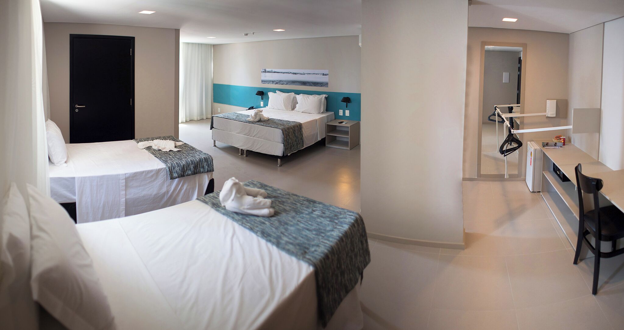 A hotel room with two beds, a desk, a chair, a bathroom, and a view of the outside.