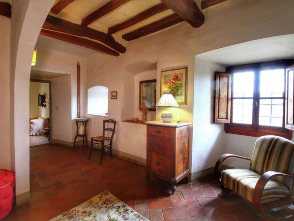 Una habitación acogedora con una silla de madera, una mesa y una lámpara. Se ve una ventana con vistas al exterior.