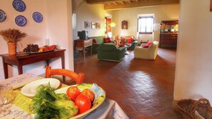A cozy living room with a dining area, featuring a wooden table set with vegetables, a green sofa, and a red armchair.