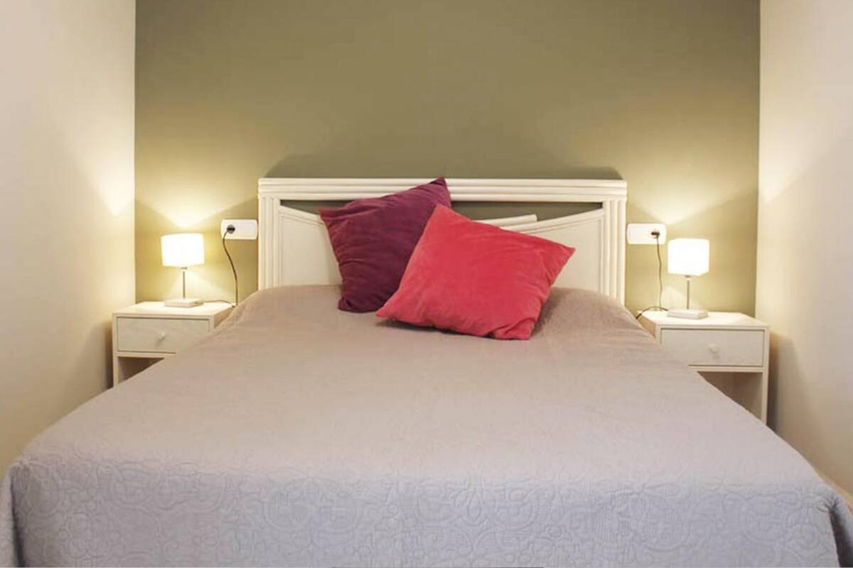 Un lit bien fait, avec une tête de lit, deux tables de chevet avec des lampes et un mur sobre.