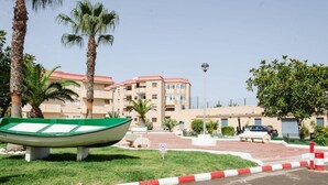 A green boat on a grassy area with palm trees and a building in the background. - Tesy II (LA MANGA)