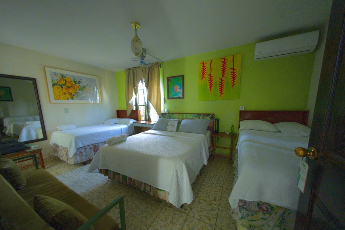 Habitación de hotel con dos camas individuales, un sofá, un escritorio y un espejo.