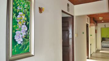 A hallway with a framed painting of flowers, a wooden door, and a bed with a green wall in the background.