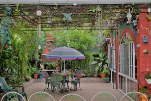 An outdoor patio with a table and chairs, surrounded by potted plants and a colorful umbrella. - Hotel Oasis (San Salvador)