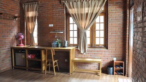 A room with a brick wall, wooden desk, chair, and a small shelf with shoes. - Trinity Family Inn (Nyaungshwe)
