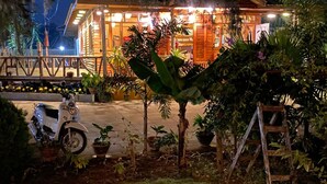 A well-lit building with a wooden exterior and a paved entrance area. There are several potted plants and a scooter parked outside. - Trinity Family Inn (Nyaungshwe)