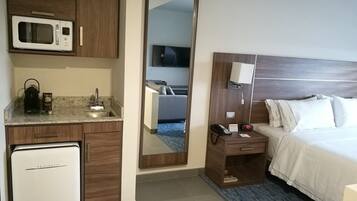 A hotel room with a bed, a bedside table with a lamp, a microwave, a coffee maker, and a mini-fridge.