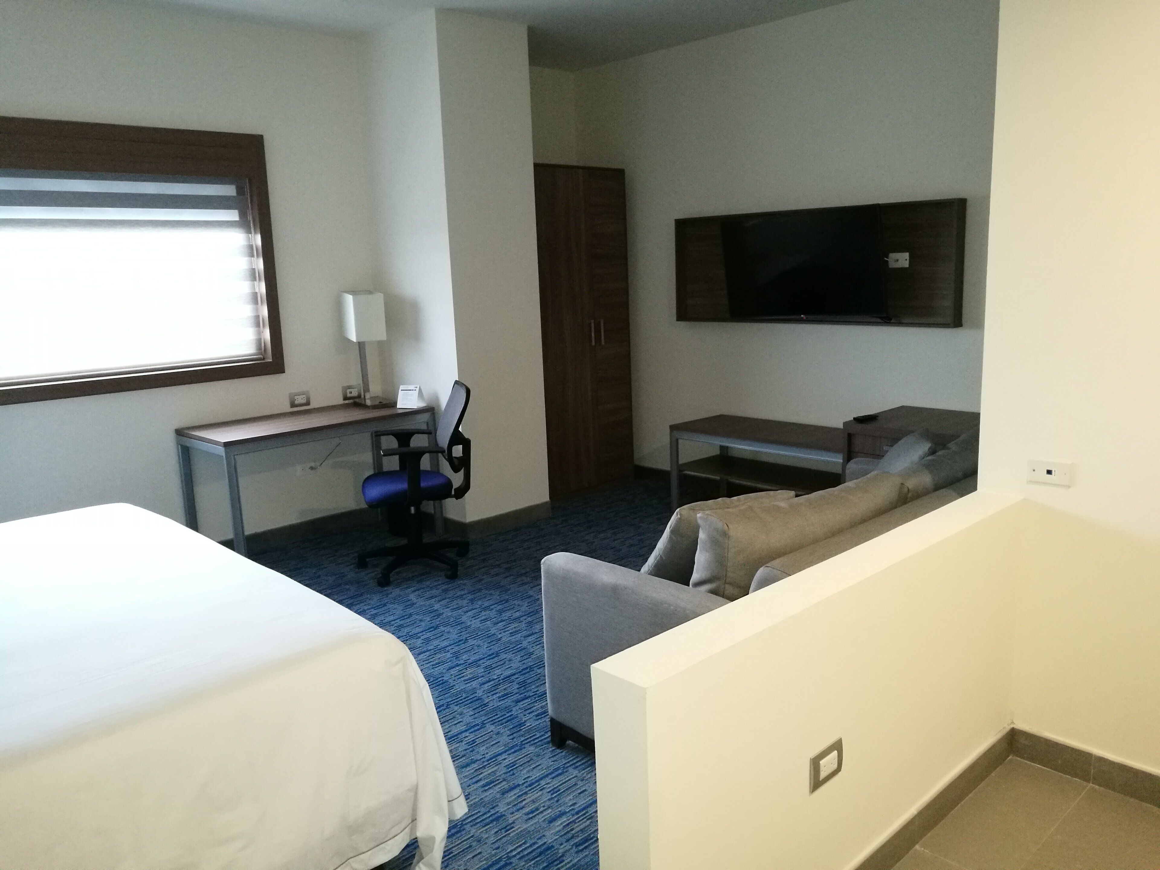 A hotel room with two beds, a desk, a chair, a sofa, a TV, and a wardrobe.