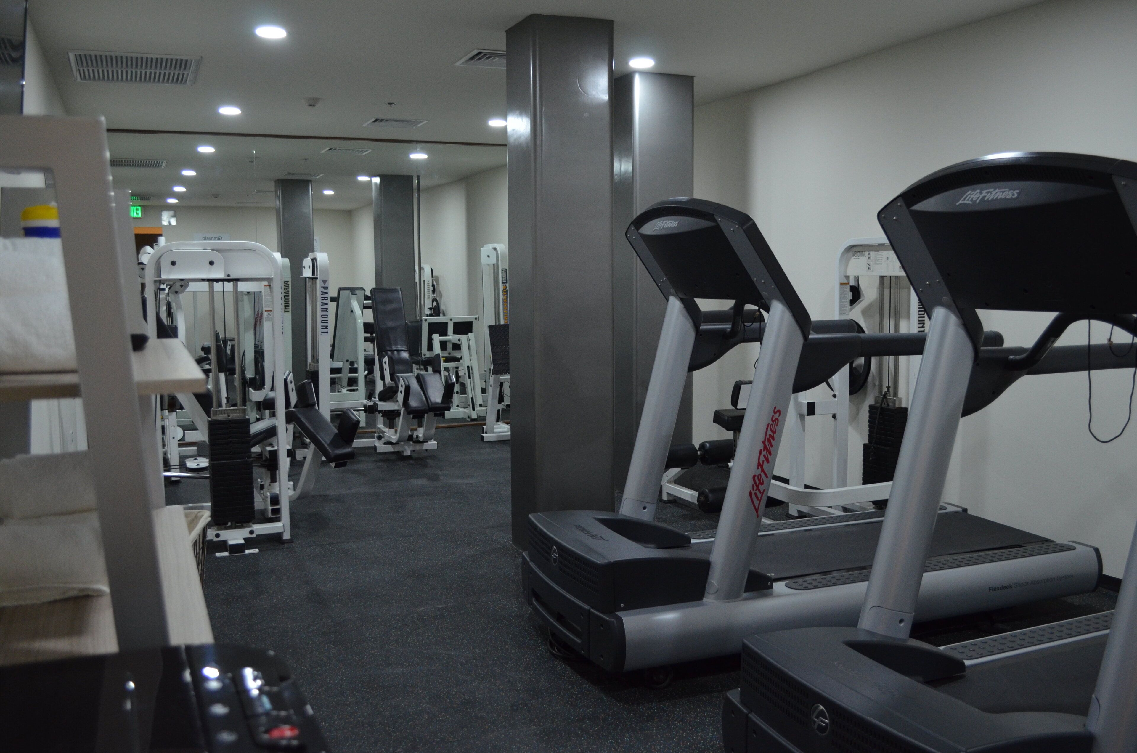 Un gimnasio con cintas de correr, máquinas de pesas y un muro con espejos.
