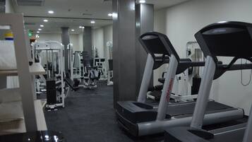 Un gimnasio con cintas de correr, máquinas de pesas y un muro con espejos.