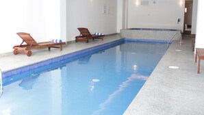 A swimming pool with two wooden lounge chairs and a small seating area. - Holiday Inn Express & Suites Ciudad Obregon by IHG (Cajeme)