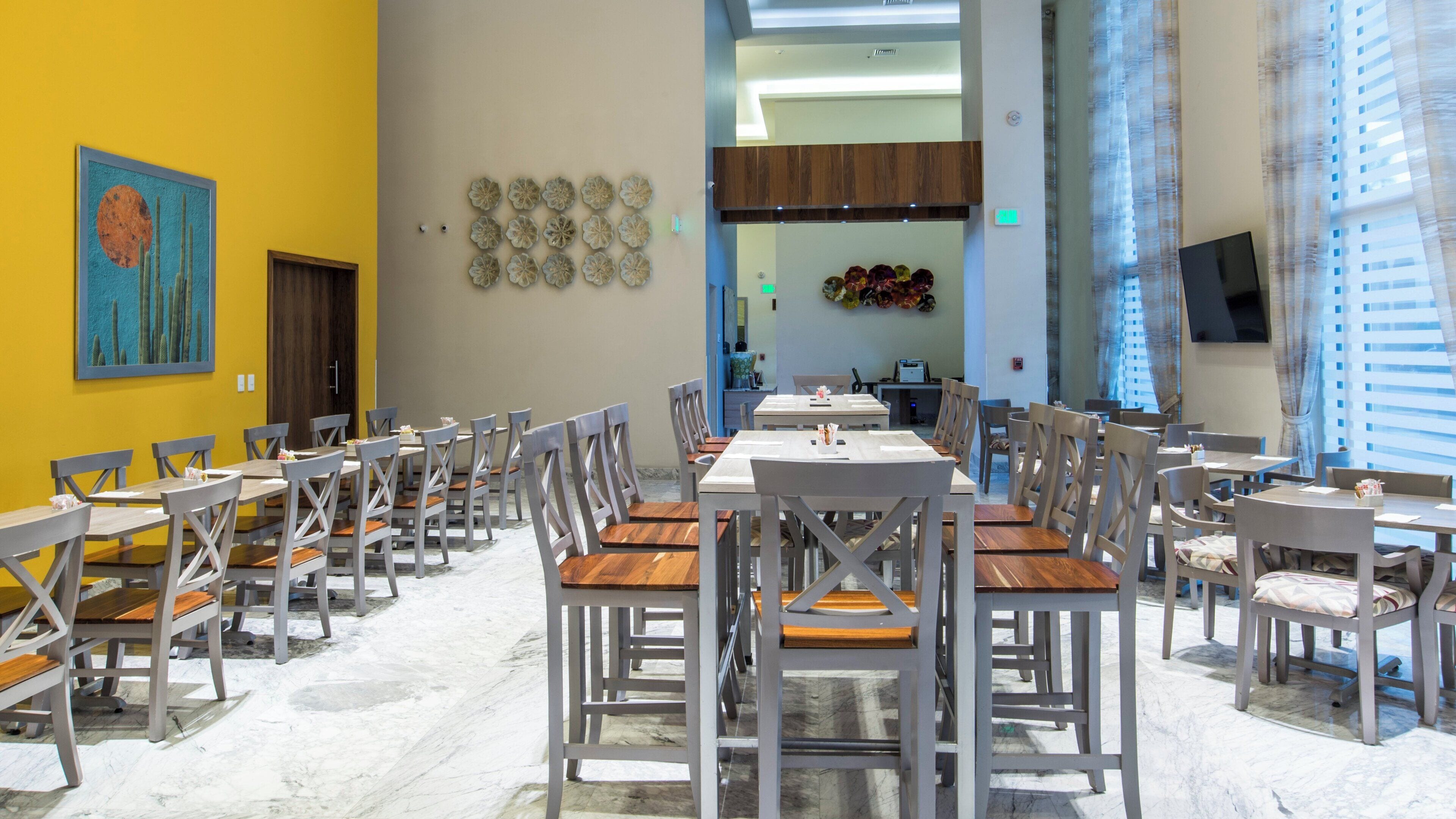 Un comedor con varias mesas y sillas, una pared amarilla con obras de arte y un diseño de interiores moderno.